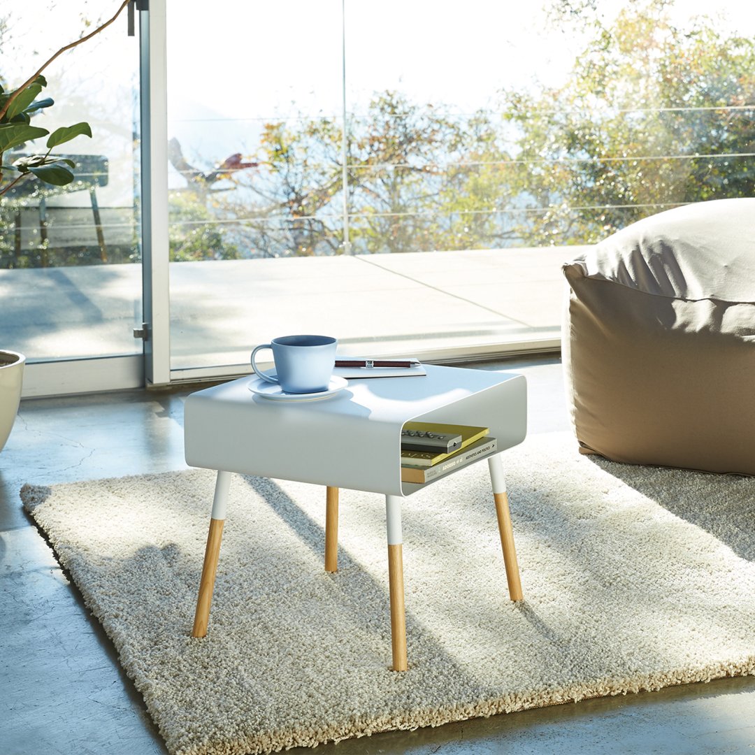 Side view of white Storage Table holding books and coffee cup in living room by Yamazaki Home.