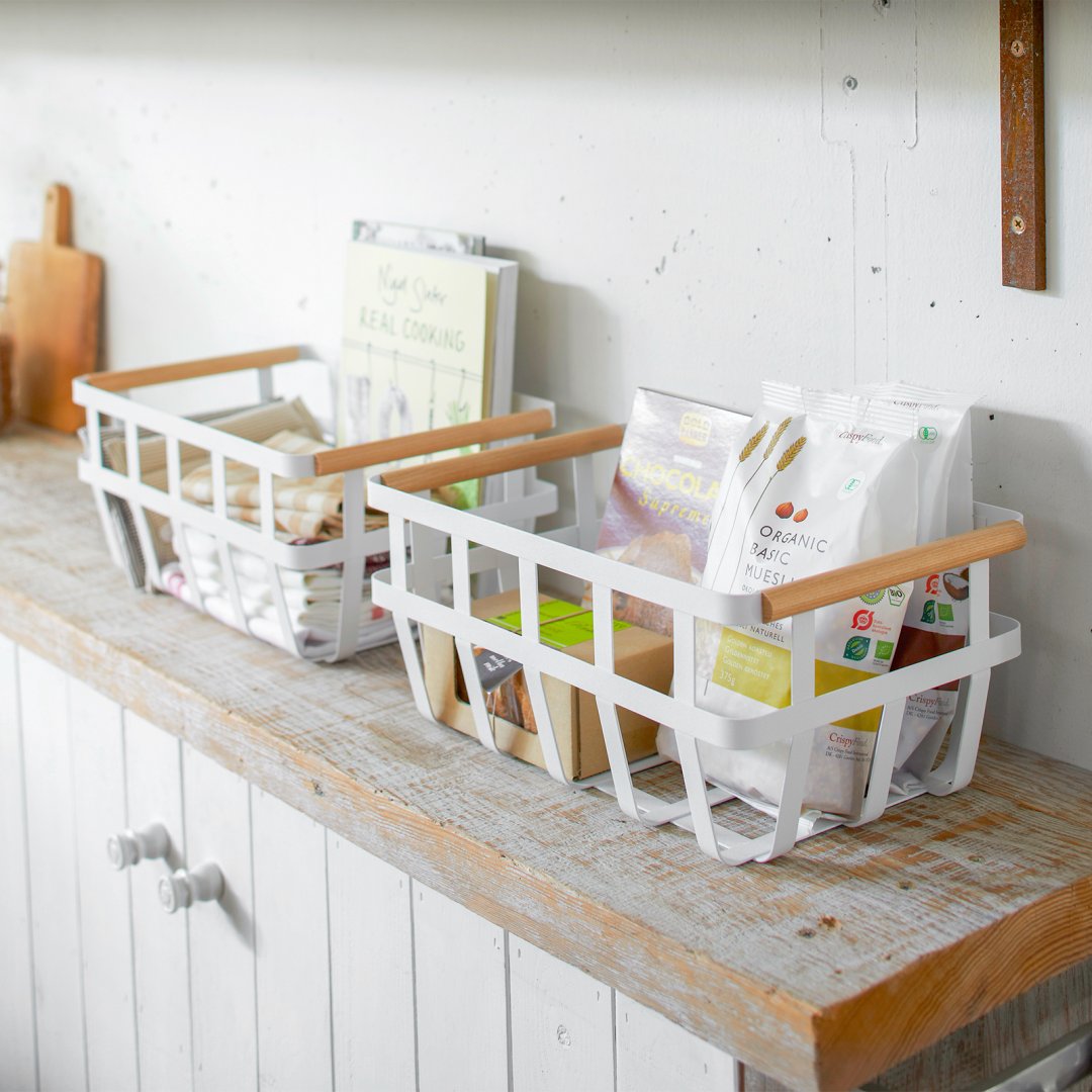 Two white Storage Baskets holding food and kitchen items on shelf countertop by Yamazaki Home.